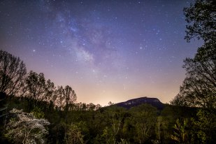 Milky Way above Moore's Knob and a dogwood in bloom, lit by the lights from the lodge at Singletree Gun and Plow
